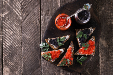 Red and black caviar in small silver spoon on a wood background with black bread ,food concept