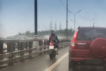 Girl with red hair in a helmet rides her motorcycle on the pavement on a rainy day.