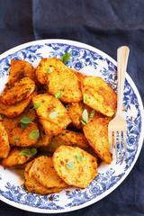 Round slices baked potatoes with spicy condiments and herb leaves, overhead shot