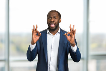 Black businessman gesturing OK. Young man in formal wear showing everything is allright with two...