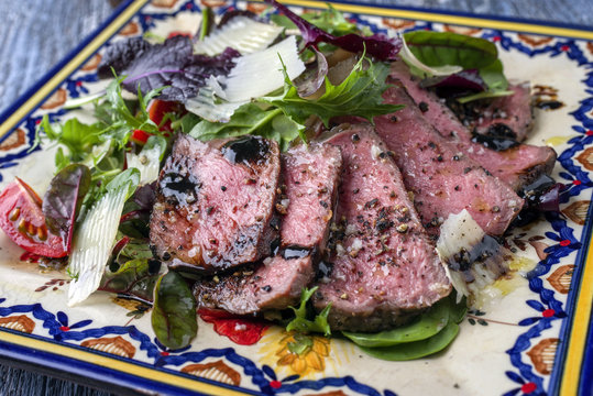 Traditional Italian tagliata di manzo steak with parmesan and salad as close-up on a plate