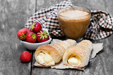Puff  pastry horns with cup of cappuccino and strawberry on wooden table