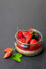 Mini  wild forest berries cheesecake in a glass pot on black stone background