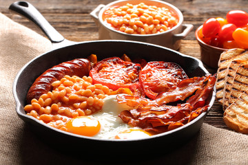 English Breakfast with sausages, grilled tomatoes, egg, bacon and beans on frying pan.