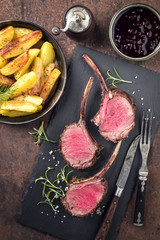 Barbecue rack of venison with roast potatoes and cranberries as top view on a black slate