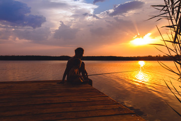 Mother and son siting on wooden dock and fishing at sunset.