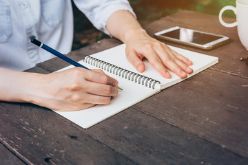 Hipster woman hand writing notebook paper in coffee shop.