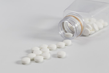 White pills pouring out of the medicine bottle on a white background