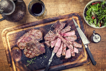 Two barbecue dry aged wagyu porterhouse steaks with rocket salad as close-up on a cutting board