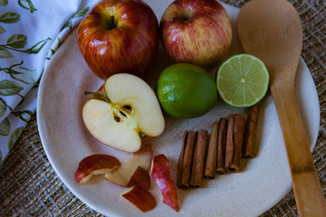 Cake ingredients: Red apples, green lemons and cinnamon sticks in a old porcelain plate with a wooden spoon.