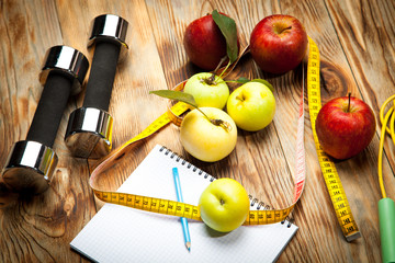 Apples, diet plan and centimeter, dumbbells on a wooden background