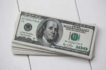 A stack of hundred dollar bills American dollars on white wooden background