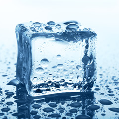 Transparent ice cube on blue glass with water drop