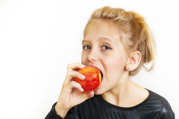 The young girl eats a delicious peach and smiles