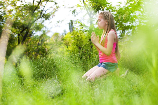 A young girl prays in the park standing on her knees