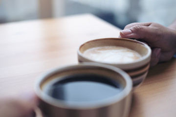 Close up image of two people clink coffee cups on wooden table in cafe
