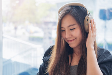 Closeup image of a beautiful Asian woman enjoy listening to music with headphone in modern cafe with feeling relax and happy