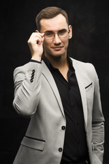The young man in a gray suit and glasses on a dark background.