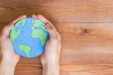 Ecology concept, holding a paper globe map painted blue and green, wooden background.