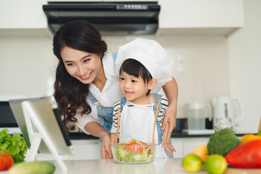 Happy family in the kitchen. Mother and child daughter are preparing the vegetables and fruit.