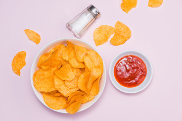 Concept of unhealthy food. Cheese and onion potato chips with hot chilli sauce on pink background.