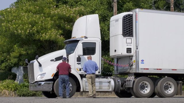 Driver meets with insurance agent, or other official with electronic notepad, for inspection of truck engine. Wide view from side of parked white truck on summer day. 4K