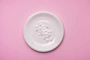 Pills served as a healthy meal. Drug capsule on white plate on pink background