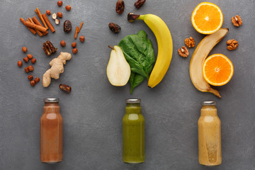 Detox smoothies with ingredients in glass bottles on gray background.