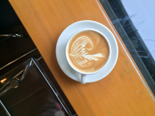 Top view of cup of hot milk coffee with rosetta latte art on wooden table in cafe / coffee shop with fresh morning light