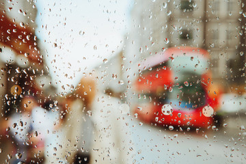 Raindrop on glass and red London bus lights background.