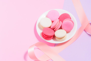 Homemade Colorful macaroons or macaron on White plate with pink ribbon on pink and purple background