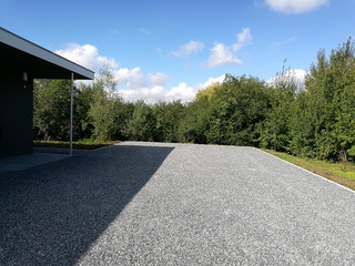 Mit grauem Schotter bedeckter Parkplatz vor blauem Himmel mit weißen Wolken im Sommer bei...