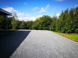 Großer Parkplatz mit grauem Schotter in einem Neubaugebiet im Sommer bei Sonnenschein am Waldrand...