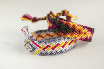 Fototapeta premium Two simple handmade homemade natural woven bracelets of friendship on white background, rainbow colors, checkered pattern