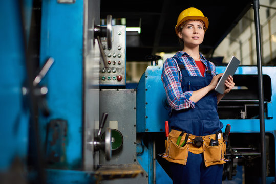 Talented Young Engineer Wearing Protective Helmet Holding Digital Tablet In Hands While Working At Manufacturing Plant