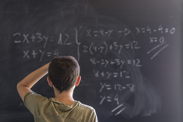 Schoolboy solving a problem on a blackboard.