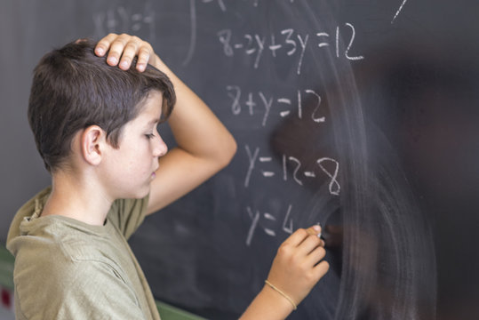 Schoolboy solving a problem on a blackboard.