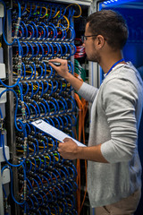 Back view portrait of young man connecting wires in server cabinet while working with supercomputer...