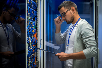 Side view  portrait of young man standing by server cabinet while working with supercomputer in...