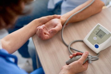Close-up shot of unrecognizable physician measuring blood pressure of male patient during check-out at office