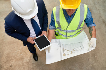 High angle view of unrecognizable foreman and architect studying blueprint while having working...
