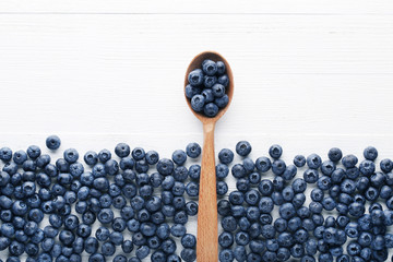 Ripe blueberries with wooden spoon on white wooden table