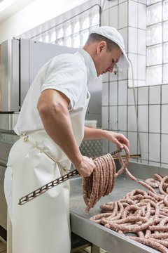 Butcher putting sausages on beam in butchery