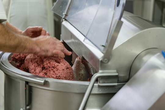 Butcher grounding meat in grinder machine to make sausages