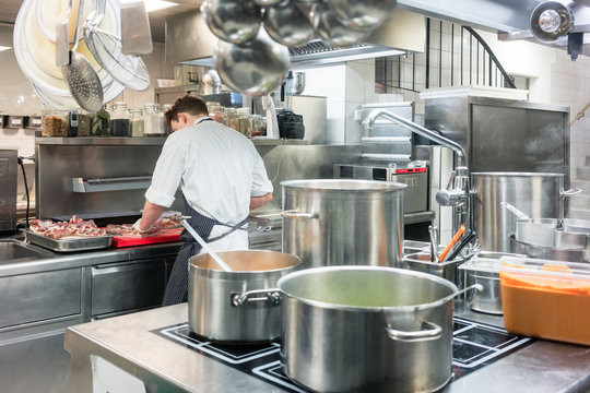 Rear view of a master chef preparing red meat on the counter of a commercial kitchen