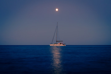 Full moon over the pinarello bay with cool reflection on the sea and a sailing ship.