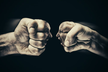 Two fists with a male and female face collide with each other on black background. Concept of confrontation, competition, family quarrel etc. - obrazy, fototapety, plakaty