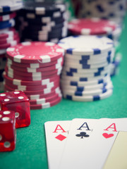 three aces and red cubes with poker chips on green table