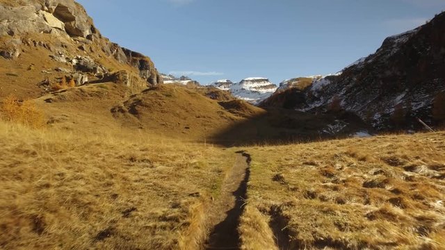 POV walking on fall field path to creek and snowy mounts.Sunny autumn day Hiking in colorful red forest wild nature mountain outdoors.Alps Devero.4k point of view establishing video
