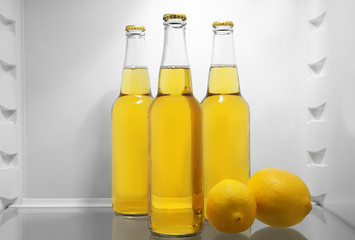 Bottles of lemonade with fresh lemons in fridge
